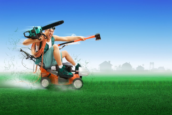 crazy workman covered with instruments driving lawn mower over green grass
